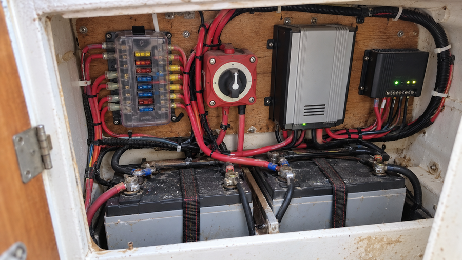 Open sailboat electrical compartment with house batteries, protected distribution, and charging equipment
