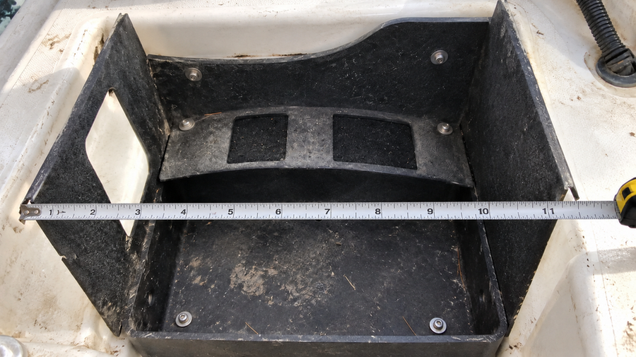 Tape measure spanning an empty battery tray in a fiberglass boat