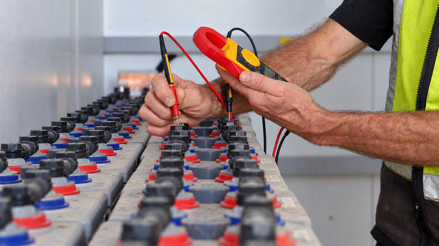 Technician comparing current across parallel battery branches with a clamp meter