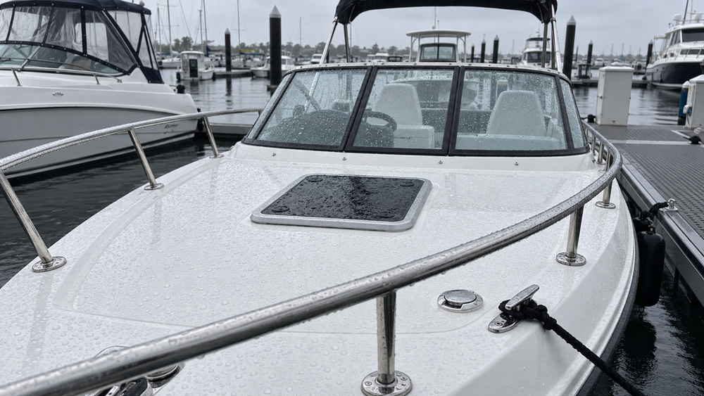 Rain beading across the white fiberglass deck of a small motorboat at a marina.